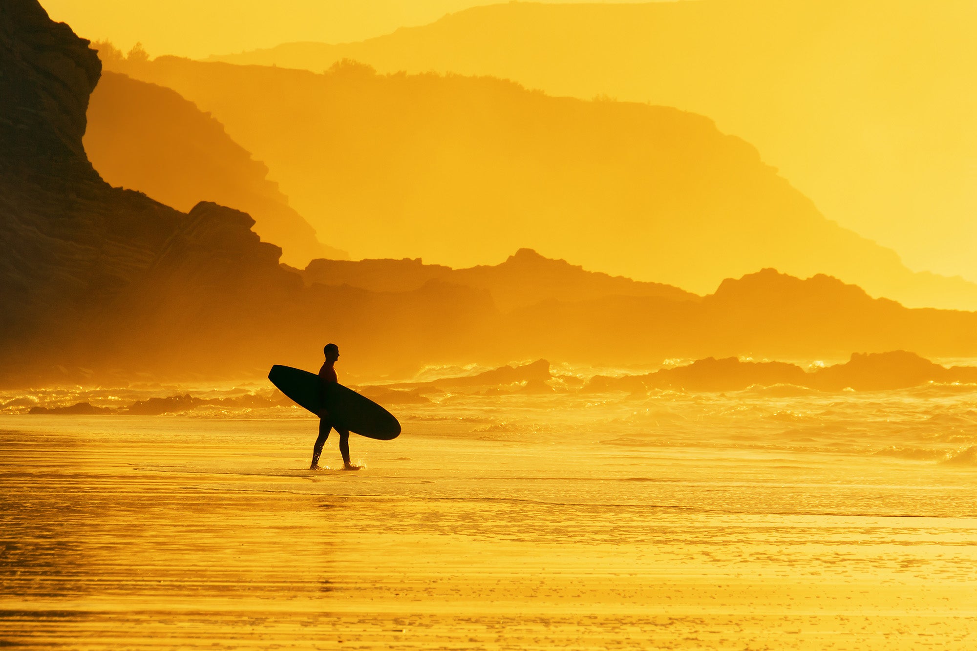Surfer holding board on beach at sunset