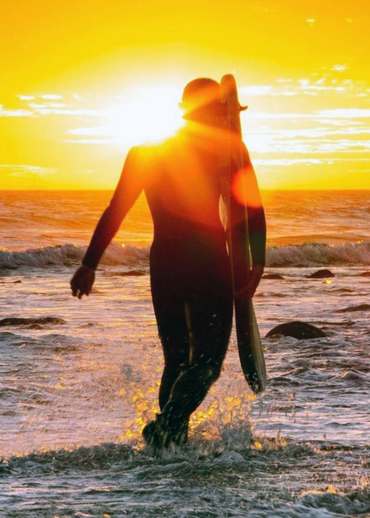 Surfer walking on beach with sunset 